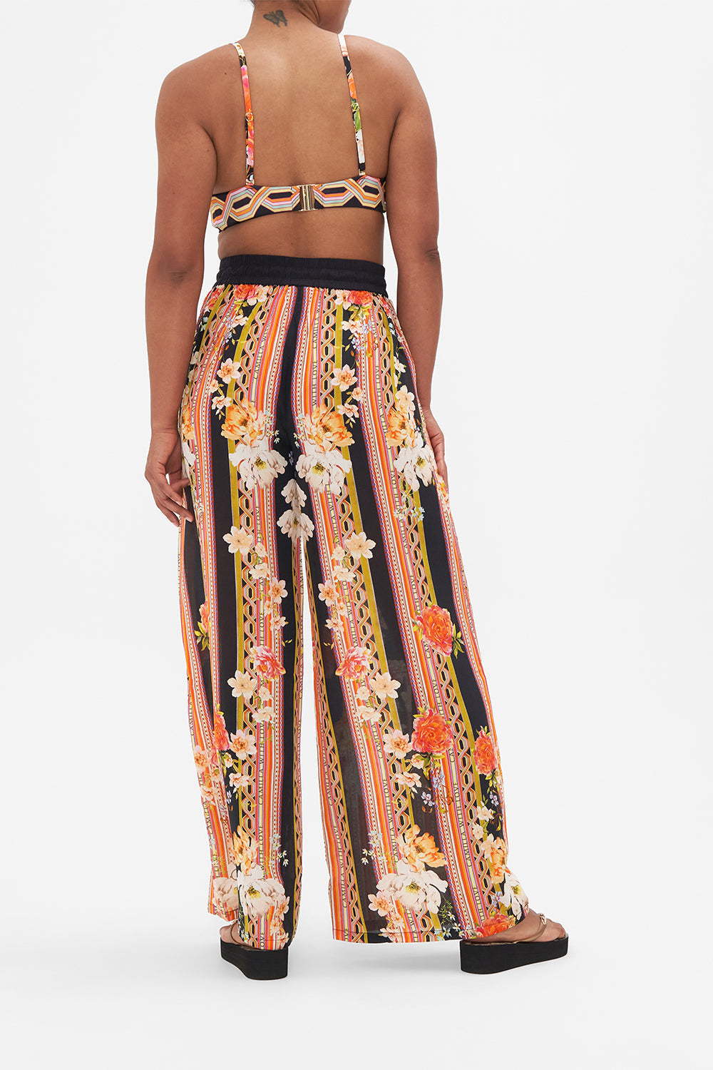 Back view of model wearing CAMILLA floral silk pants in Secret History print