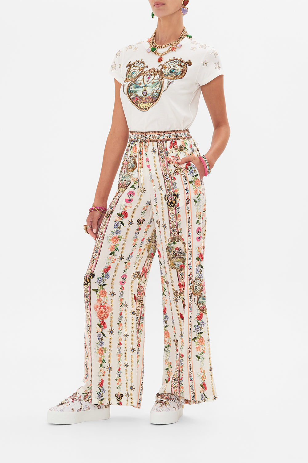 Side view of model wearing Disney x CAMILLA silk pants in Minnie Magic Forever print