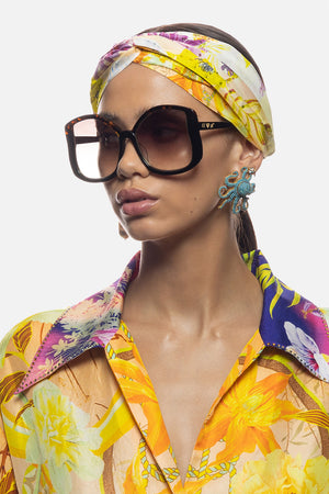 A woman with a colorful hijab and sunglasses smiles confidently at the  camera